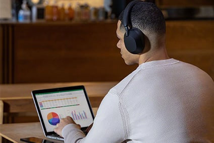 Male model working in a cafe on his laptop while wearing a pair of Sony WH-1000XM5 Noise-Canceling headphones to help him focus.